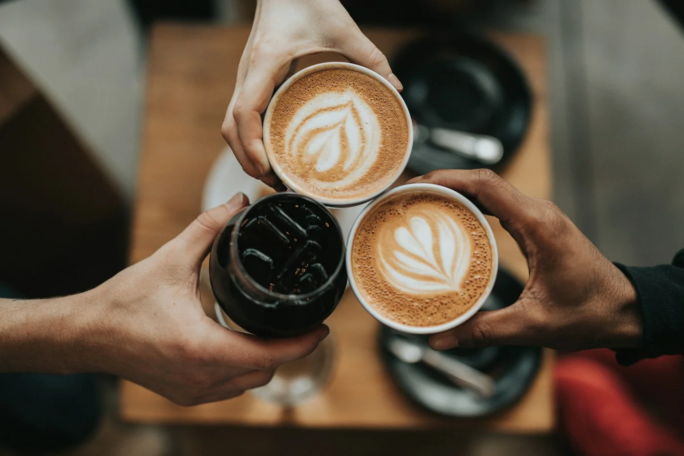 Three people bringing their coffee cups together over a table